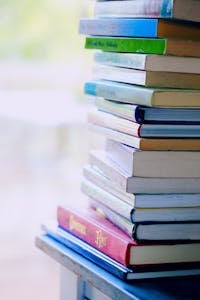 A tall stack of colorful hardcover books on a table indoors, perfect for library-themed concepts.