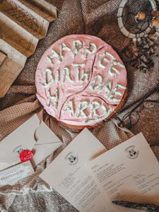 Pink birthday cake with Harry Potter theme surrounded by letters and decorations.